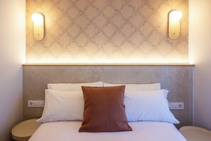 Une chambre d’hôtel avec un lit, un oreiller marron, deux appliques murales et un papier peint à motifs.