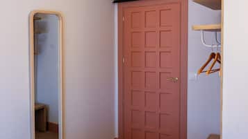 A bedroom with a bed, a wooden headboard, a red door, a mirror, and a wooden bench.