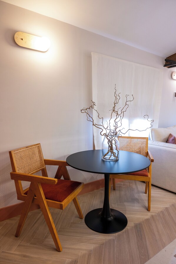 A dining area with a round table, two chairs, a vase with branches, and a wall-mounted light.