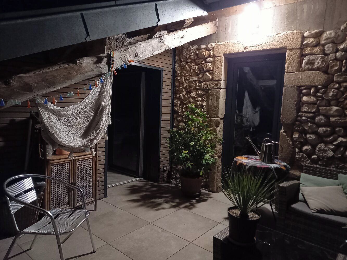 An outdoor patio area with a stone wall, a hammock, a potted plant, a metal chair, and a table.