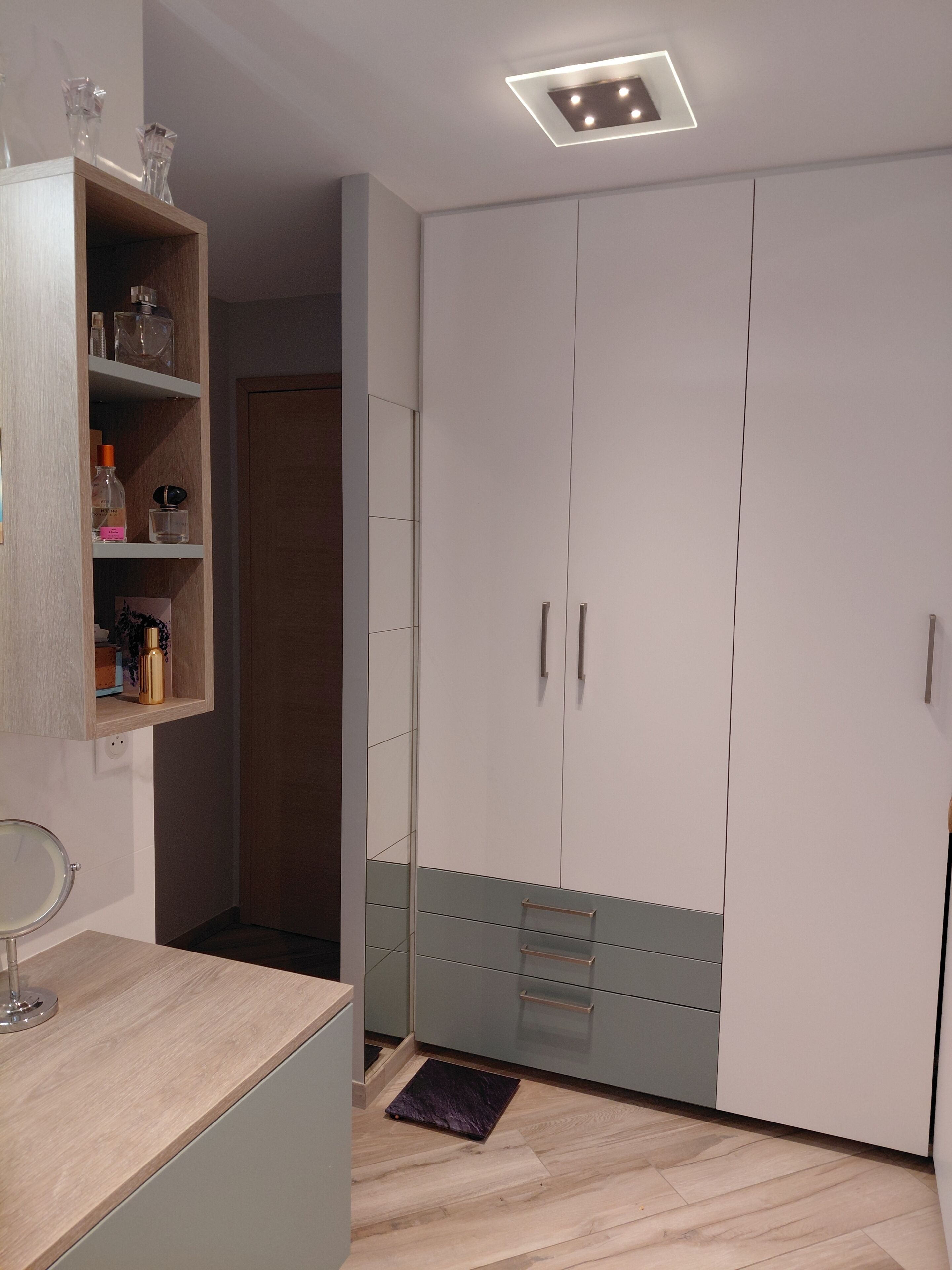 Une salle de bain moderne avec un meuble-lavabo en bois, un miroir et une étagère contenant des articles de toilette.