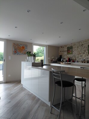 A modern kitchen with a large island, bar stools, and a stone wall. - THE TERRACE (Saint-Laurent-en-Royans)