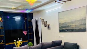 A modern living room with a sectional sofa, a chandelier, a large painting, and a dark blue entertainment unit. - Spacious 4-bedroom villa in pleasant Vijayawada with AC (VIJAYAWADA)