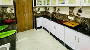 A kitchen with white cabinets, a black countertop, and a wooden door. - Spacious 4-bedroom villa in pleasant Vijayawada with AC (VIJAYAWADA)