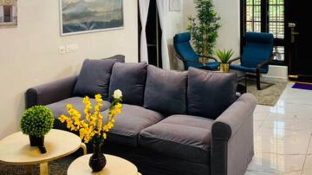 A modern living room with a grey sofa, two small round tables, a chandelier, and a large window. - Spacious 4-bedroom villa in pleasant Vijayawada with AC (VIJAYAWADA)