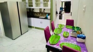 A dining area with a table set for four, a refrigerator, and a kitchen area with cabinets. - Spacious 4-bedroom villa in pleasant Vijayawada with AC (VIJAYAWADA)