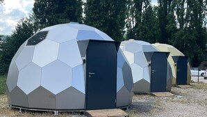 Vier geodätische Kuppelbauwerke mit Türen und Holzrampen.