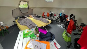 Ein Zimmer mit zwei Betten, einem Tisch mit einer Karte und einer Flasche, und Fahrrädern in der Ecke.
