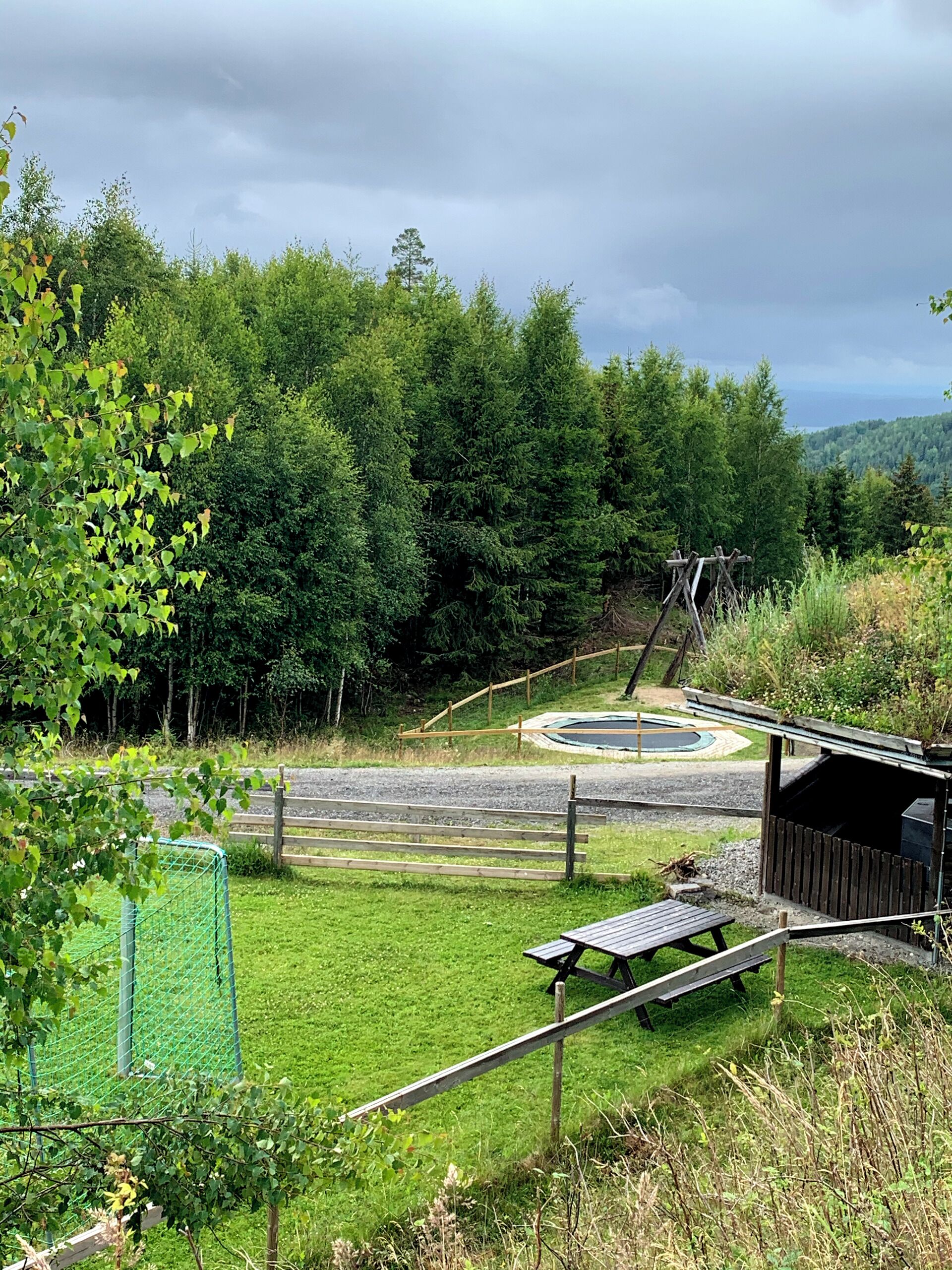 A picnic area with a wooden bench, a small shelter, and a fenced play area.
