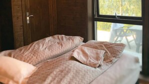 Ein Einzelbett mit einem gemusterten Bettbezug und Kissen, eine Holztür und ein Fenster mit Blick auf Bäume.