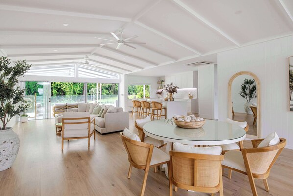 A spacious living area with a glass dining table, wicker chairs, a sofa, and a ceiling fan.