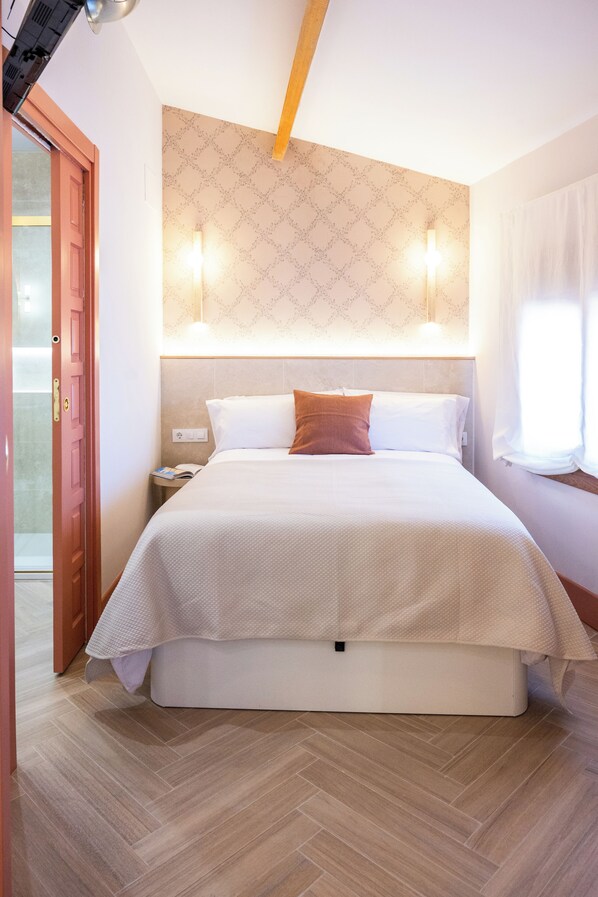 A hotel room with a bed, a nightstand, a wall-mounted light, and a door.