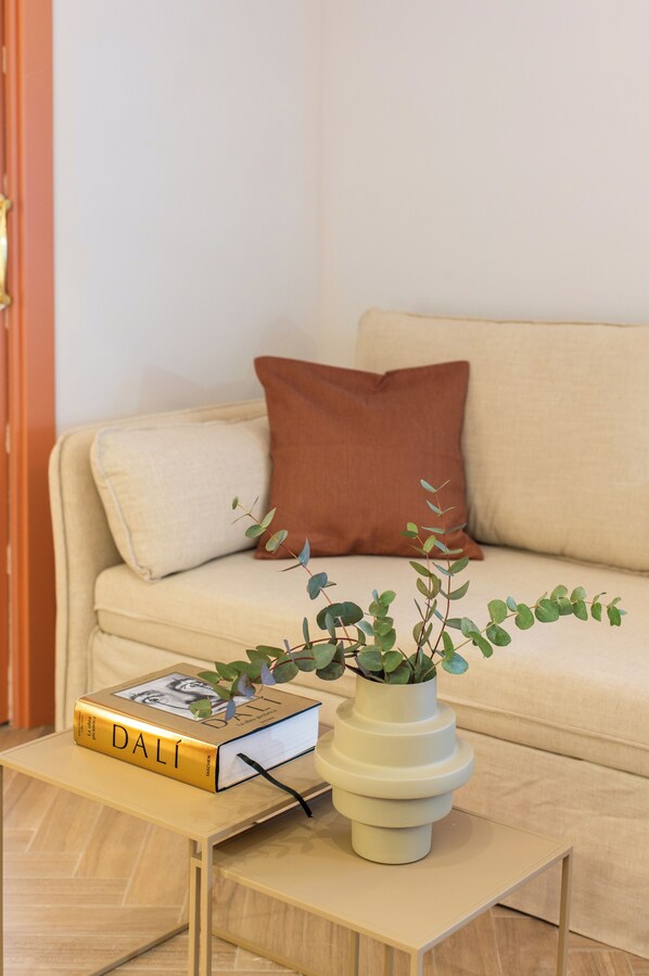 A living room with a sofa, a coffee table, a book titled 'DALÍ,' and a potted plant.
