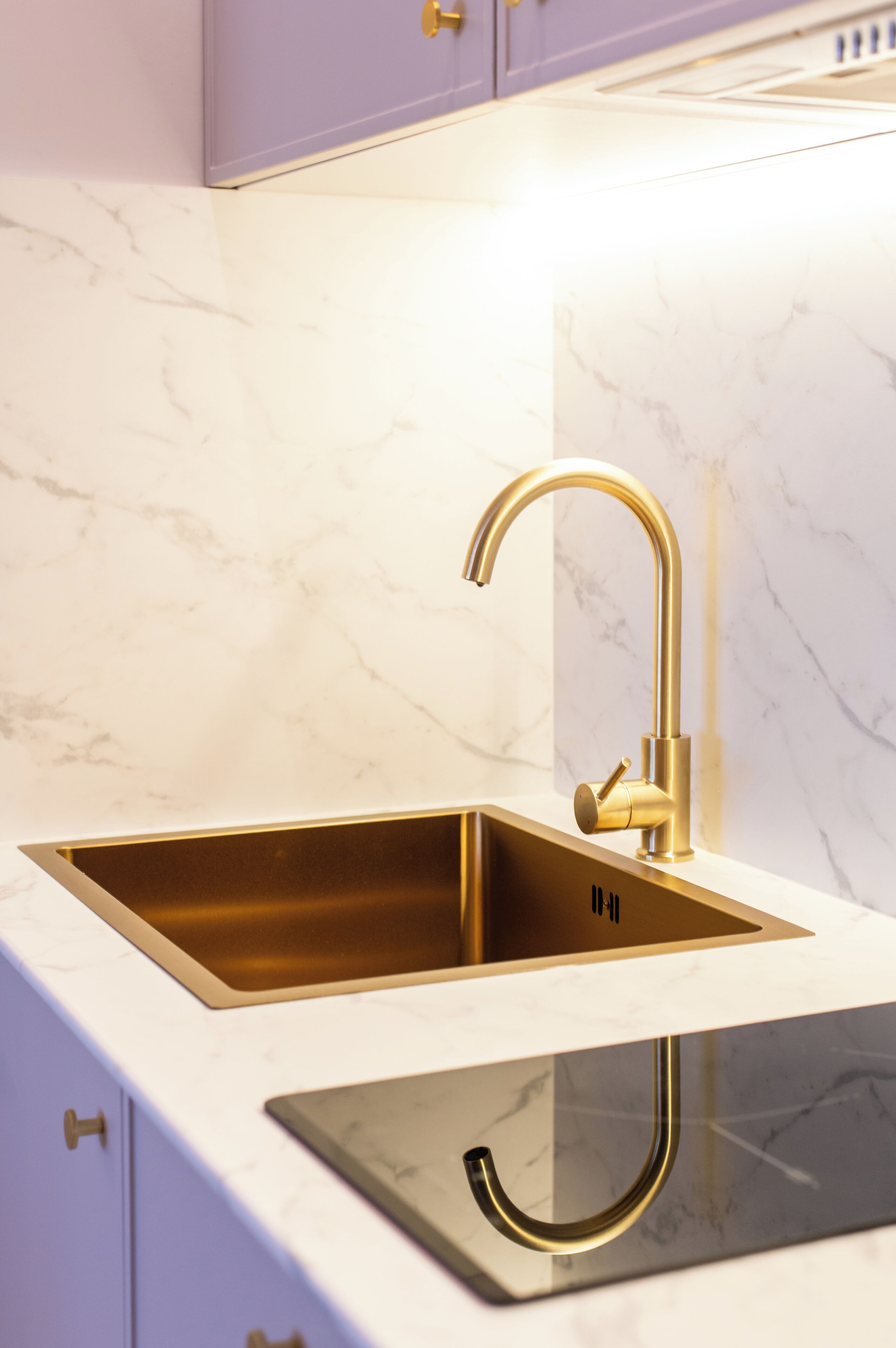 A kitchen with a gold faucet, white marble countertop, and a black stove.