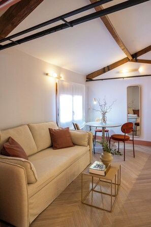 A living room with a sofa, a coffee table, a dining table with chairs, a mirror, and a window with curtains.
