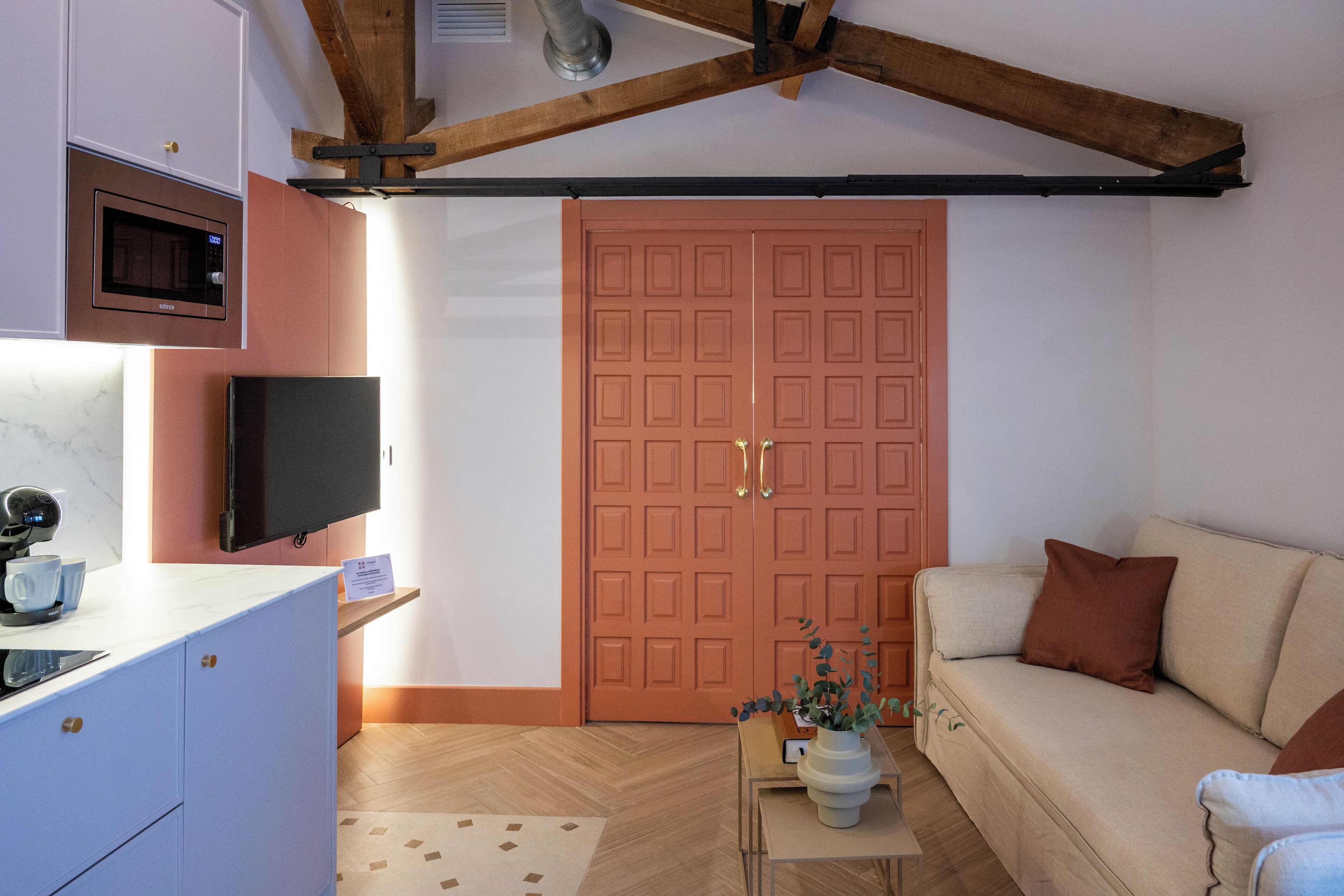 Ein gemütlicher Wohnraum mit Küchenzeile, Fernseher, Sofa und Holzboden.