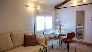 A living room with a sofa, a dining table, chairs, a mirror, and a plant. - 4Duques Apartments (Cáceres)