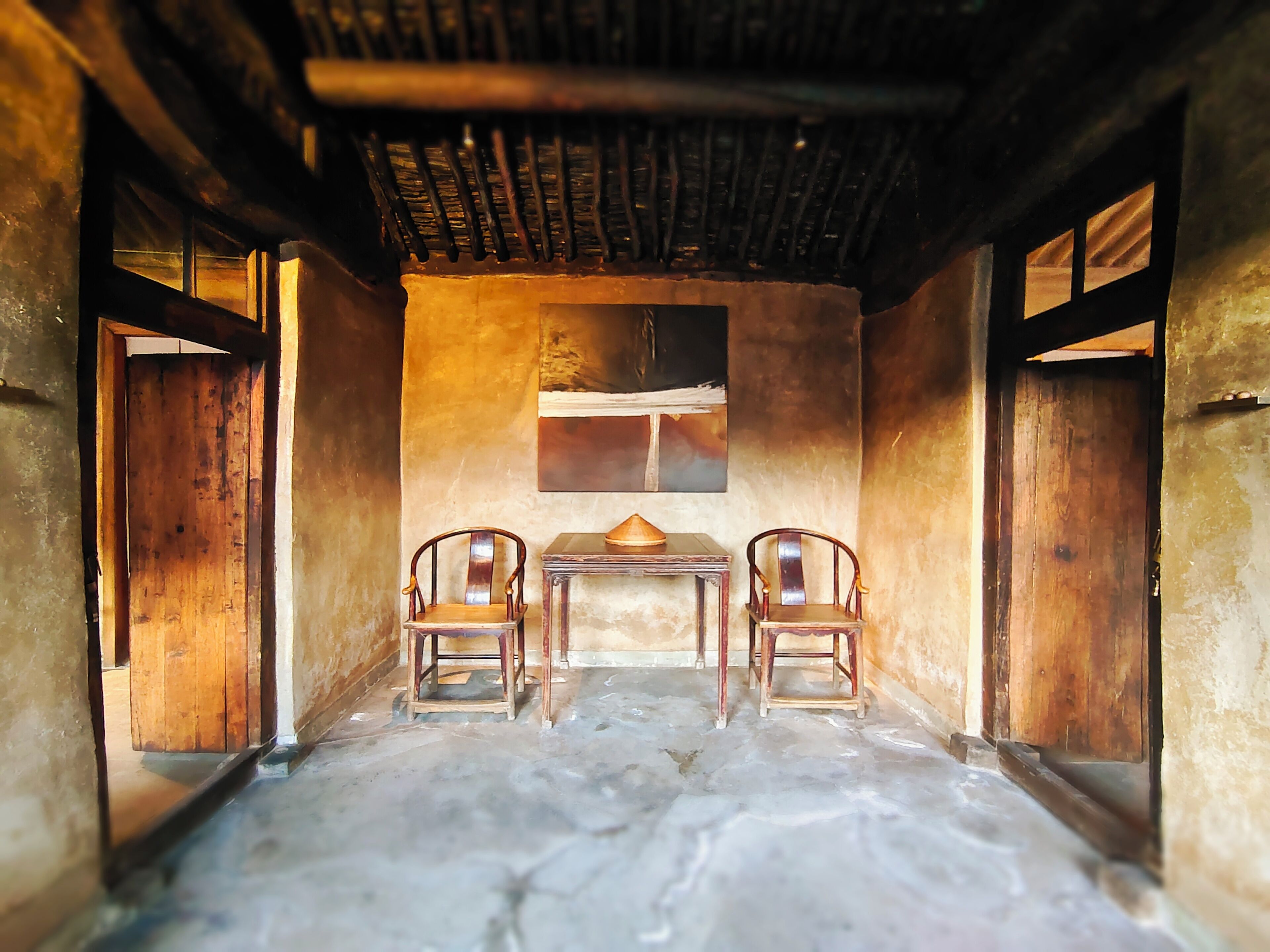 A room with two wooden chairs, a small table, and a painting on the wall.