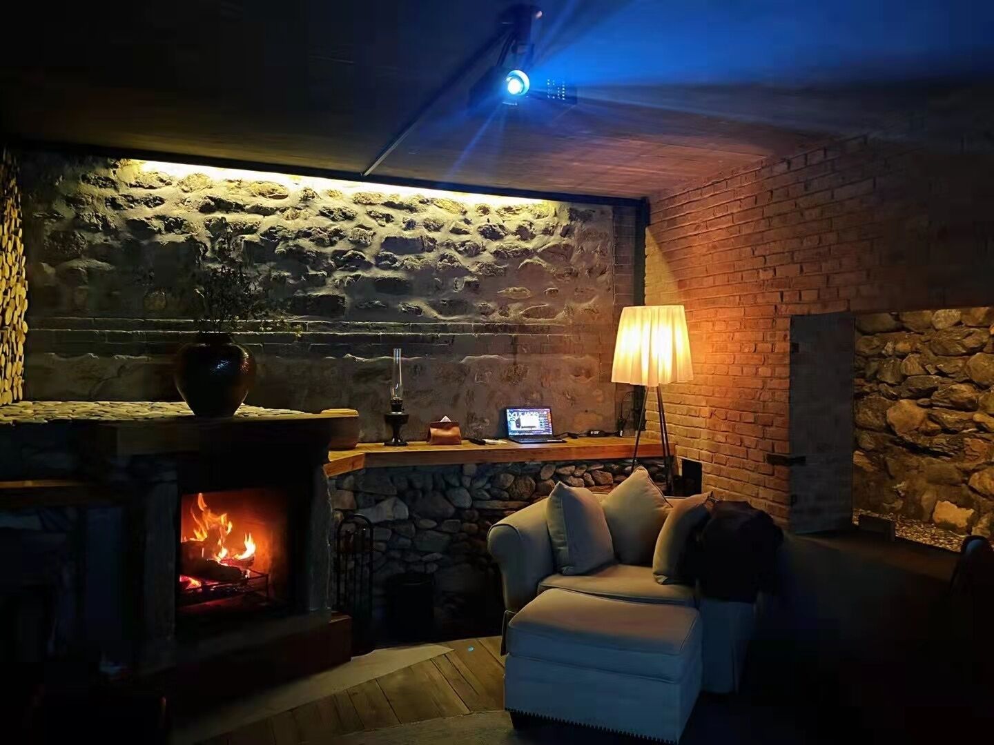 A cozy room with a stone wall, a fireplace, a sofa, and a lamp.