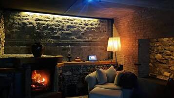 A cozy room with a stone wall, a fireplace, a sofa, and a lamp.