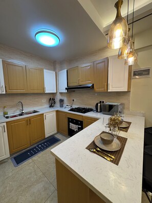 A modern kitchen with wooden cabinets, a built-in oven, a microwave, and a central island with a bowl and utensils. -     Cozy Nairobi Nest in South C • Ideal for Business & Leisure (Nairobi)