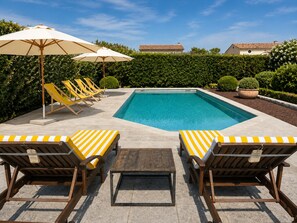 Ein Schwimmbecken mit Liegestühlen und Sonnenschirmen, umgeben von Hecken und Kübelpflanzen.