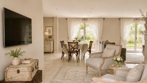 Un salón amplio con comedor, un televisor montado en la pared y un ventanal con cortinas.