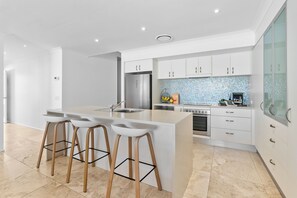 Eine moderne Küche mit Kochinsel, Barhocker, einem Edelstahlkühlschrank und einer gefliesten Spritzschutzwand.