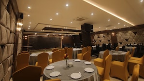Un salón de banquetes con mesas redondas, sillas amarillas y una pared de mármol.
