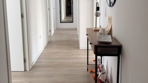 Un corridoio con pavimento in legno, pareti bianche e uno specchio alla destra.