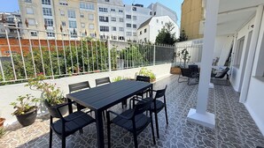 Una terrazza sul tetto con tavolo e sedie, piante in vaso e vista sugli edifici circostanti.