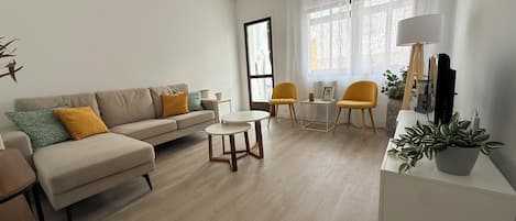 A modern living room with a sofa, two chairs, a coffee table, and a TV stand with a plant.