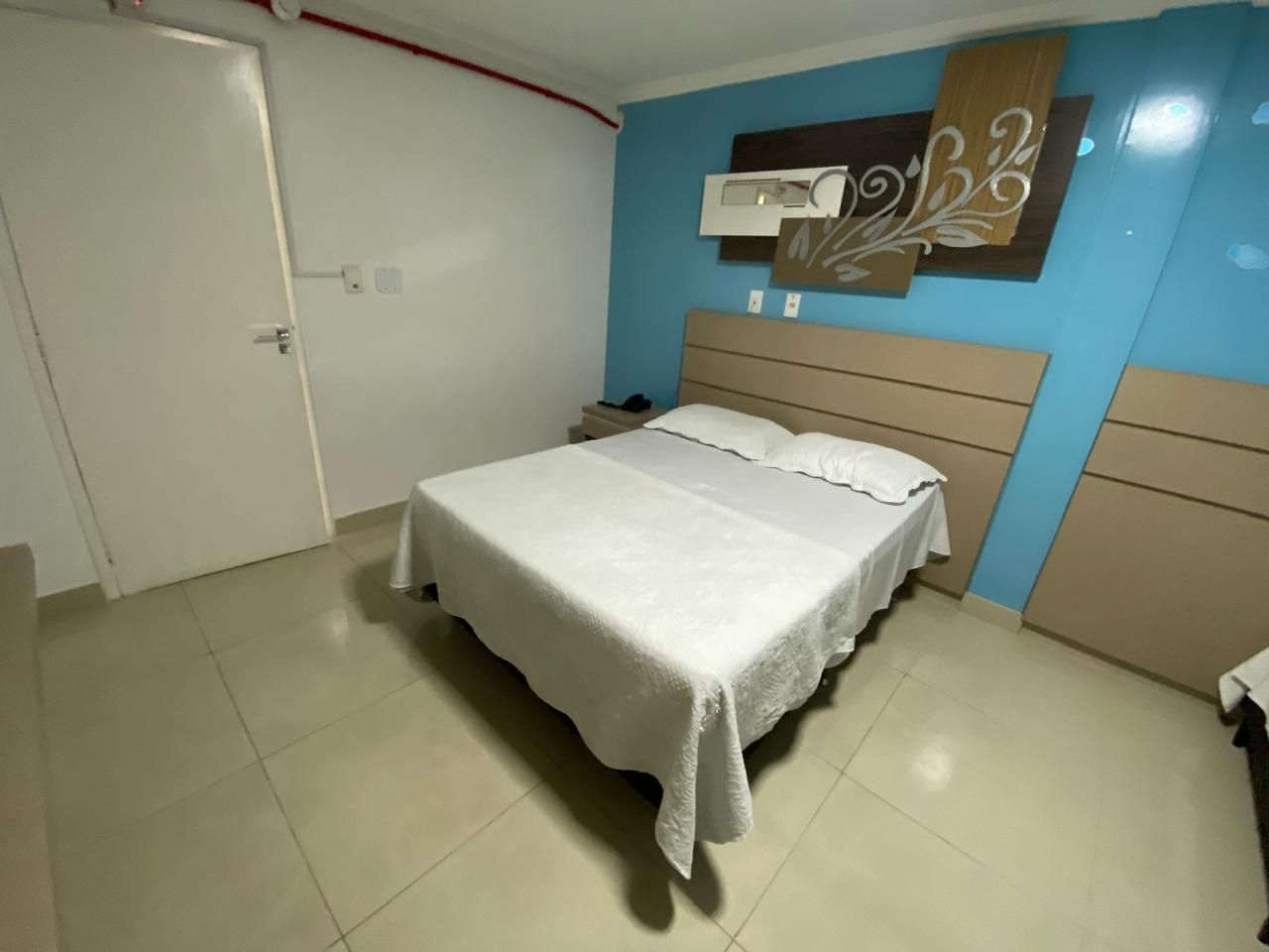 A bedroom with a bed, a nightstand, a wall-mounted air conditioning unit, and a door.