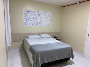 A single bed with a grey bedspread in a room with a plain wall and a white door.