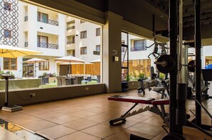 Ein Fitnessraum mit Trainingsgeräten, großen Fenstern und Blick auf einen Innenhof mit Sitzgelegenheiten.
