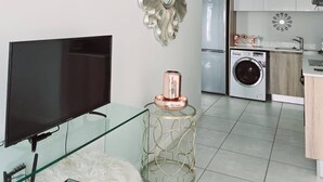 Un salon moderne avec un téléviseur à écran plat, une table basse en verre et un tapis blanc moelleux.