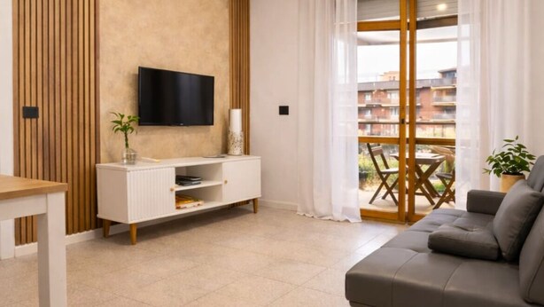 Ein modernes Wohnzimmer mit Flachbildfernseher, einer Couch, einem weißen Schrank und einem großen Fenster mit Vorhängen.