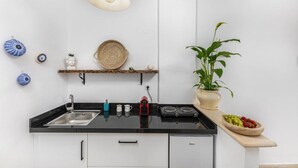 Une cuisine avec un plan de travail noir, des armoires blanches, un luminaire suspendu, une plante en pot et des objets décoratifs accrochés au mur.