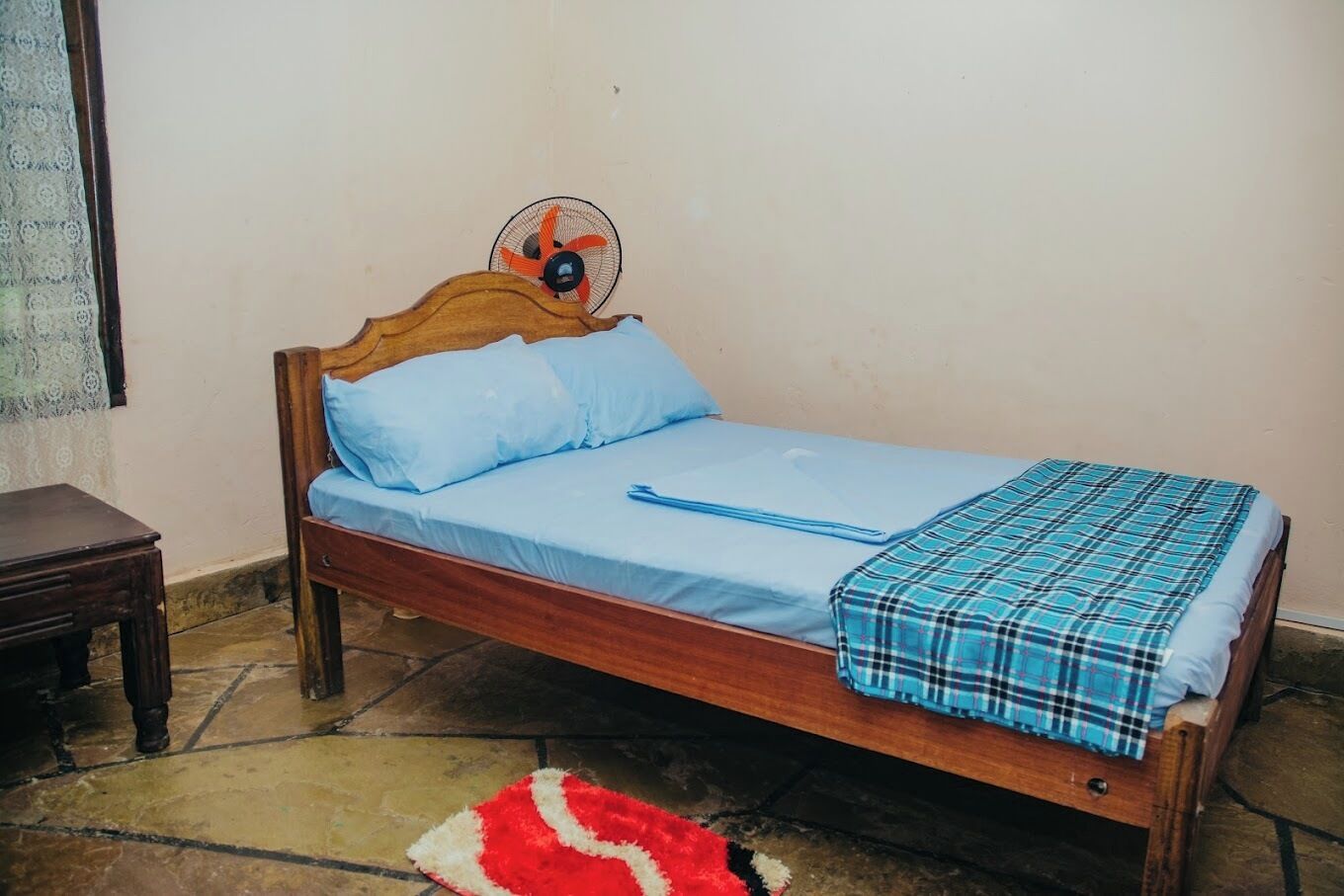 A single bed with a wooden headboard, a blue mattress, and a plaid blanket.
