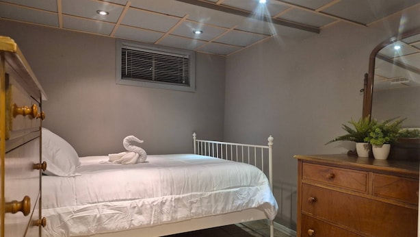 A bedroom with a bed, a dresser, a mirror, a window with blinds, and a ceiling with recessed lighting.