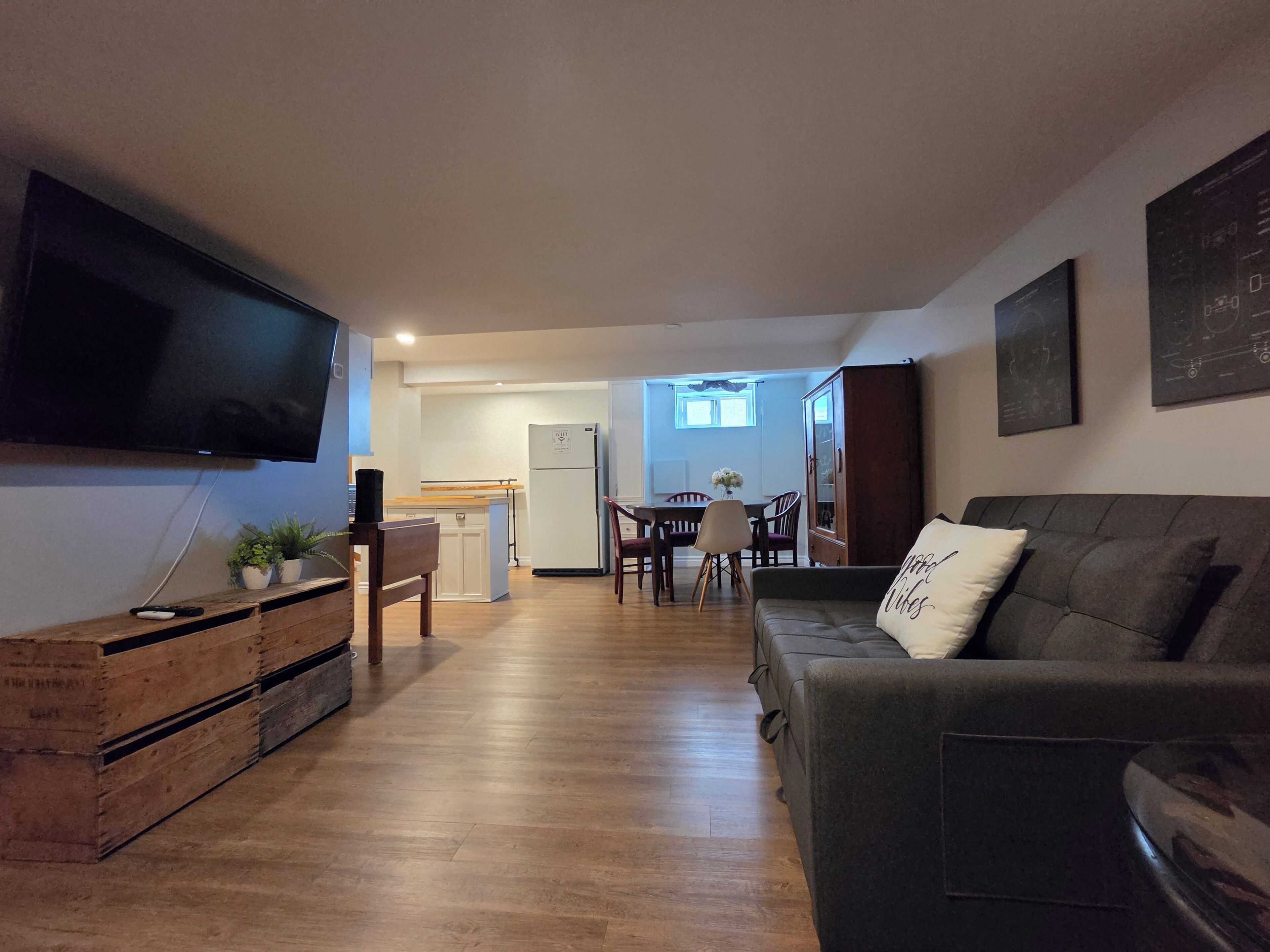 A living room with a flat-screen TV, wooden flooring, a sofa, and a dining area with a table and chairs.