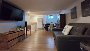 A living room with a flat-screen TV, wooden flooring, a sofa, and a dining area with a table and chairs.