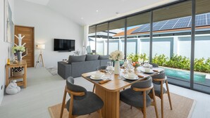 A modern living room with a dining area, large windows, and solar panels on the roof. - Seaside New 3BR Pool Villa 2 Min Walk to Bangtao Beach, Villa Belplaya Phuket (Tambon Choeng Thale)