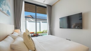 A hotel room with a bed, a TV, a window with curtains, and a view of a pool and solar panels. - Seaside New 3BR Pool Villa 2 Min Walk to Bangtao Beach, Villa Belplaya Phuket (Tambon Choeng Thale)