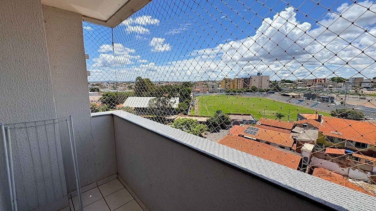 A balcony with a chain-link fence overlooking a sports field and buildings.