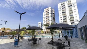 A rooftop pool area with outdoor seating and umbrellas, surrounded by tall residential buildings.