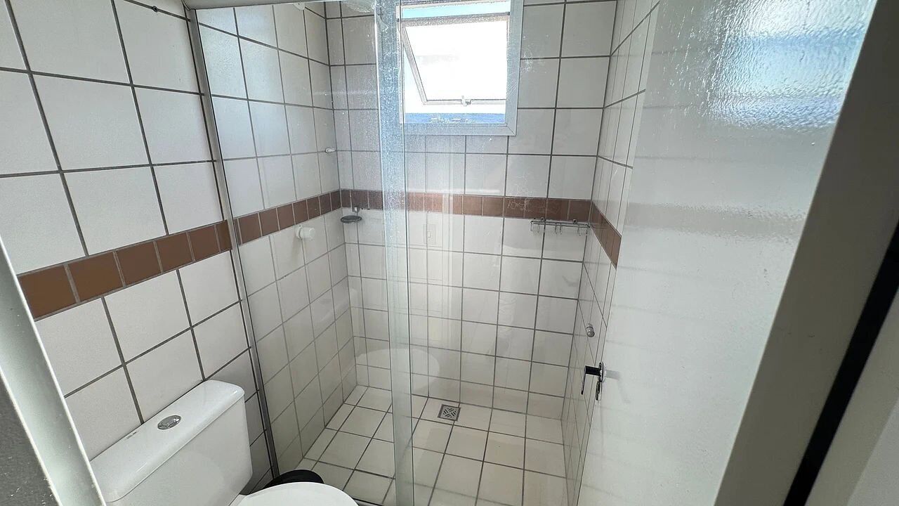 Un baño pequeño con azulejos, con ducha, inodoro y ventana.
