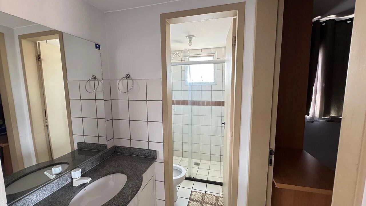 Un baño con lavamanos blanco, dos aros para toallas, ducha con puerta de vidrio y tocador de madera.