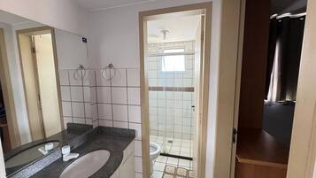 Un baño con lavamanos blanco, dos aros para toallas, ducha con puerta de vidrio y tocador de madera.