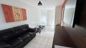 A modern living room with a black leather sofa, a glass dining table, and a flat-screen TV. - CRCN - Aquarius Residence (Caldas Novas)